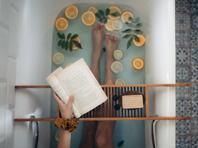 湯船にお湯をはりその中にオレンジやライムを入れて、読書をしながら入浴している女性