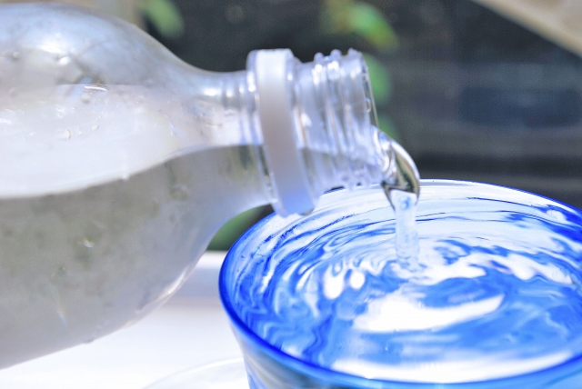 ペットボトルの水をグラスに注ぎ水がこぼれそうなようす
