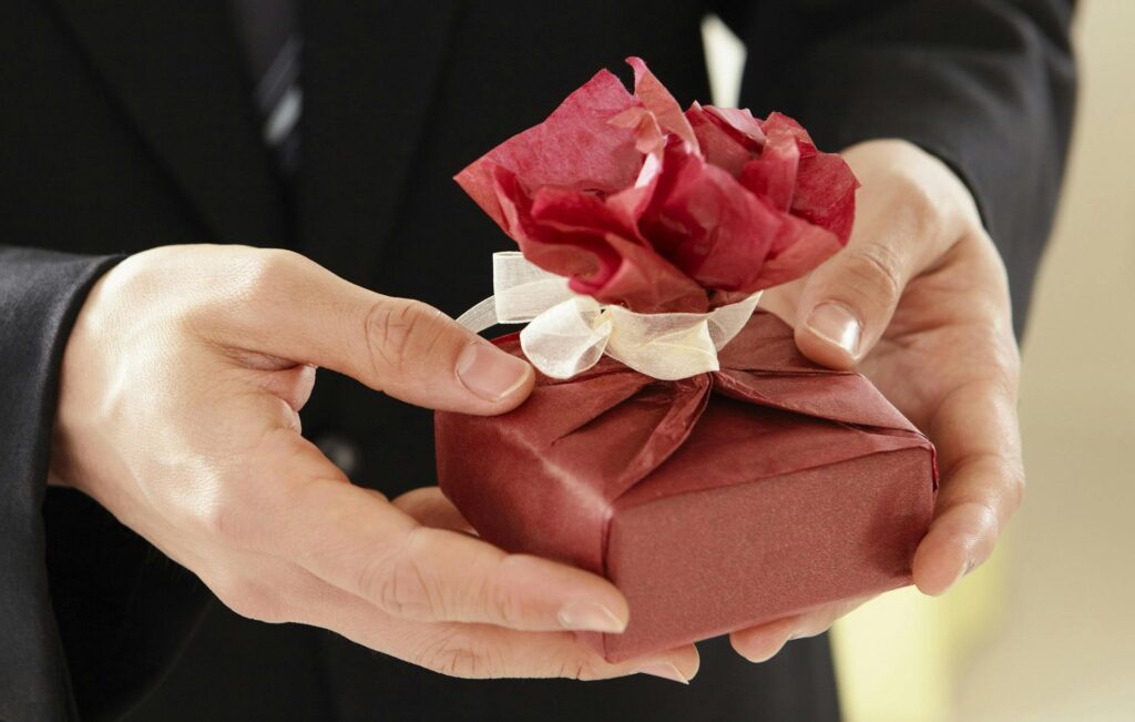 赤い包みのプレゼントを渡そうとしている男性の手