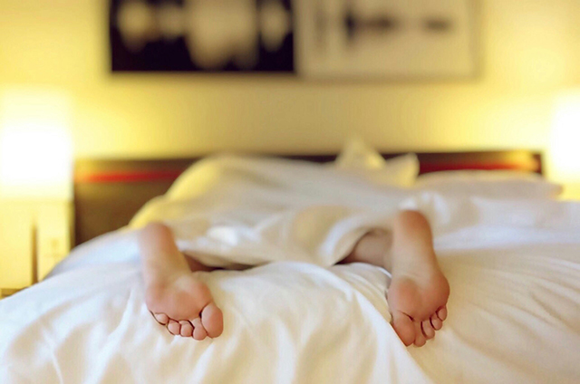足を布団から出しベッドで熟睡する女性