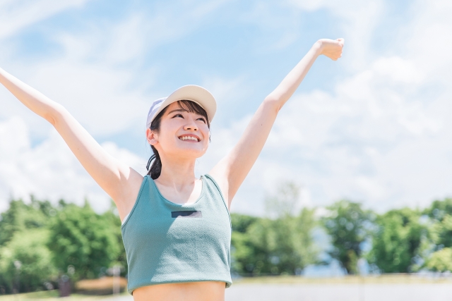 両手を上にあげ公園でリフレッシュする若い女性