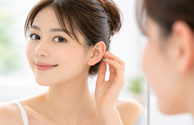 鏡を見て自分の耳元に満足している若いアジア人女性