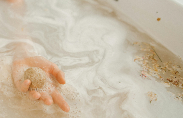 湯舟に浸かり、バスボムをてのひらにのせて溶かしている女性の手