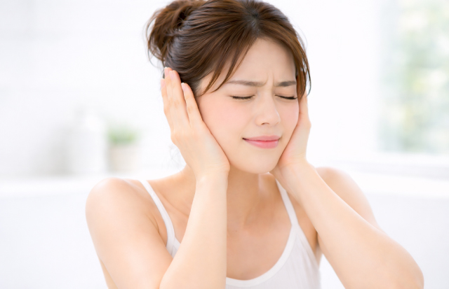 両手で両耳を手のひらで押さえ、困った表情をしている女性