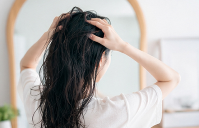 髪にヘアオイルをなじませている若いアジア人女性