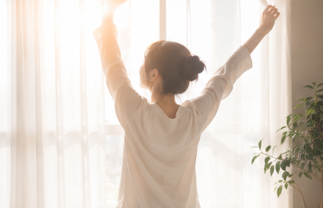 カーテンを開け朝日を浴びている若い女性