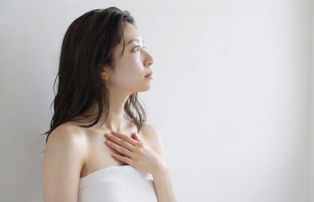 お風呂上がり、脱衣所でタオルを巻いて胸に軽く手を当てている若い女性